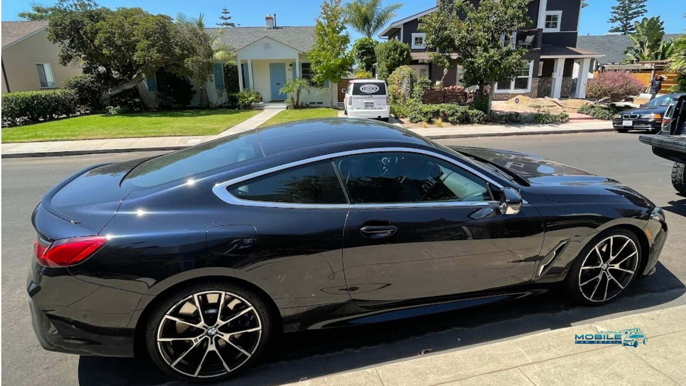 Black BMW 8 Series coupe with mirror-like finish after car wash and wax in sunny San Diego neighborhood
